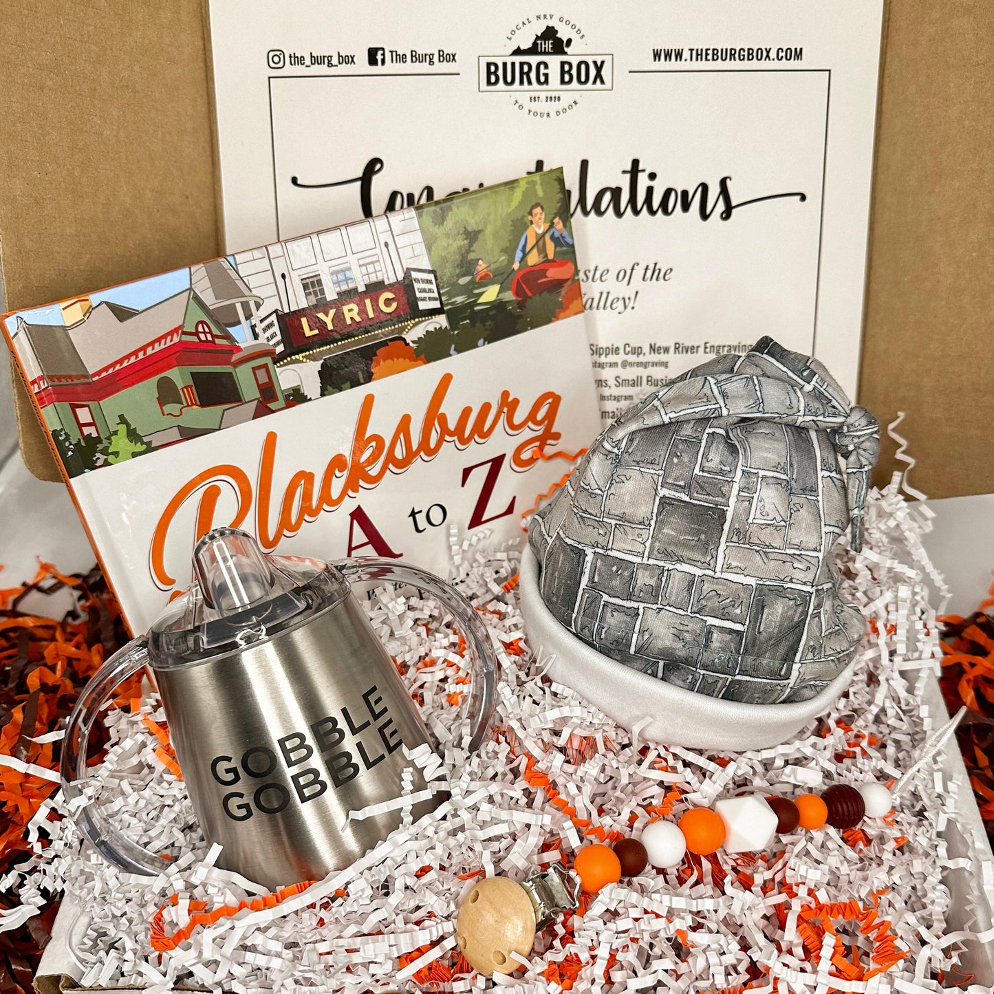 Burg Box Baby Box open with pacifier clip, stainless sippie cup, Hokie stone infant hat and Blacksburg A to Z book