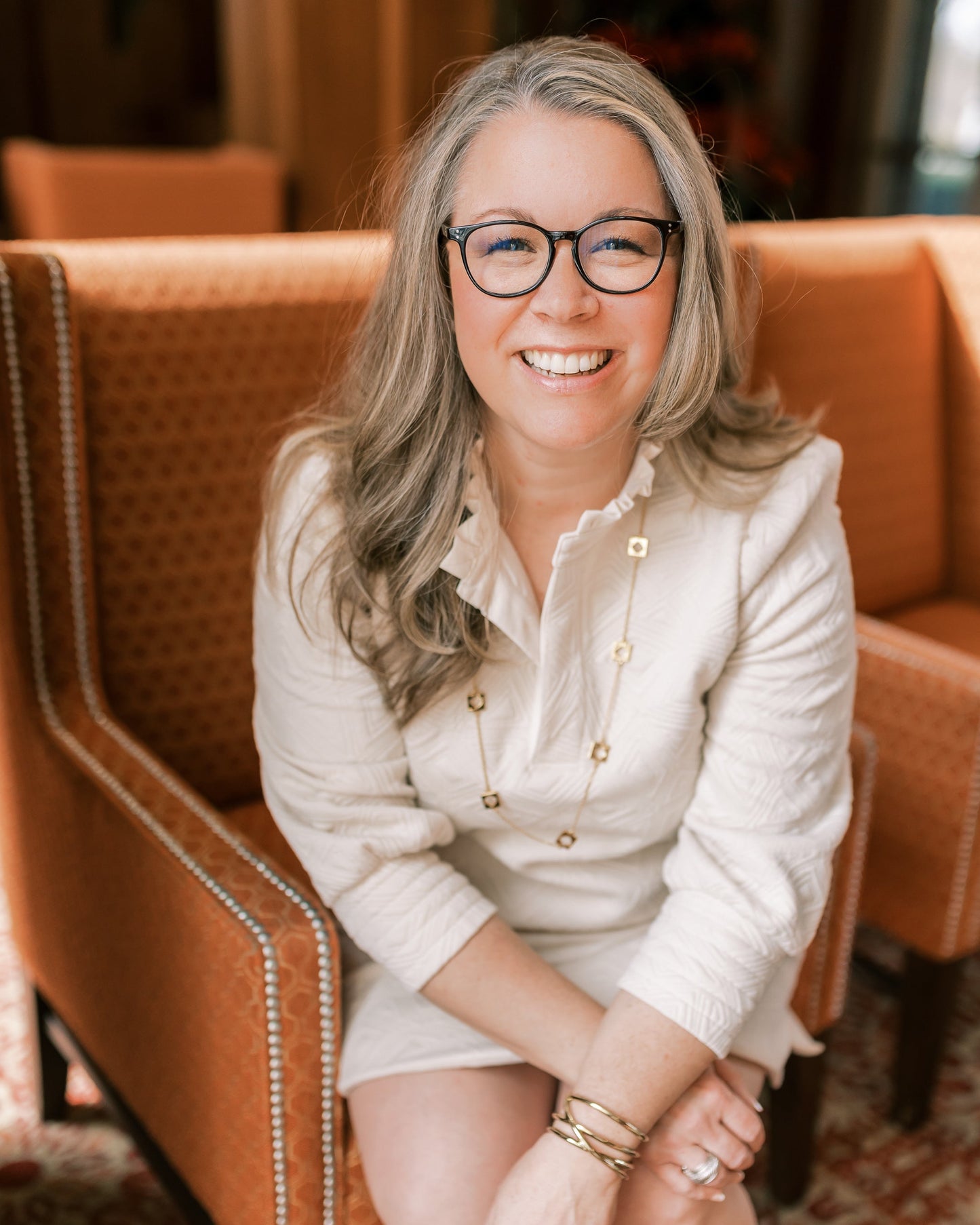 Jennifer Prevette headshot sitting in orange chair with smile